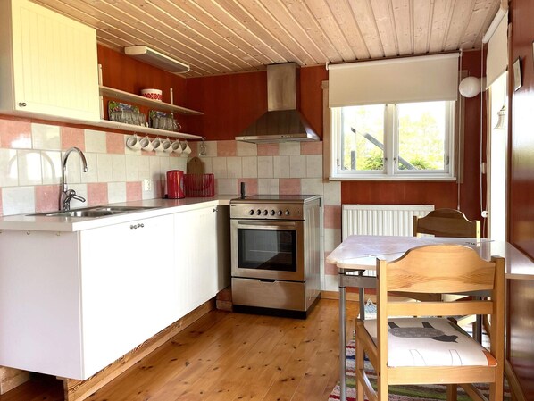 A compact kitchen with a built-in oven, a sink, and a window with blinds.