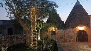 A stone building with a conical roof, a tree with a ladder wrapped in lights, and a paved courtyard. - TRULLI ALLEGRETTI (Private pool): your vacation in the heart of Puglia (Noci)