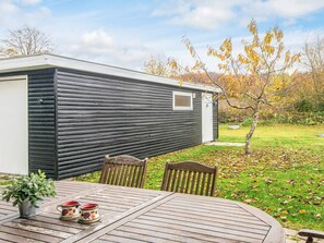 Une maison mobile à l’extérieur sombre, dotée d’une petite fenêtre et d’une terrasse avec une table et des chaises.