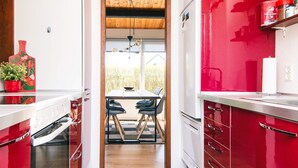 Una cocina moderna con armarios rojos, techo de madera y vista a un área de comedor al aire libre.