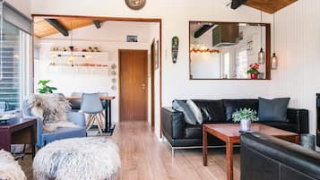 A modern living room with a wooden ceiling, a black leather sofa, a wooden coffee table, and a fluffy white ottoman.