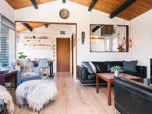 Una sala de estar moderna con techo de madera, un sofá de cuero negro, una mesa de centro de madera y un otoman blanco y mullido.