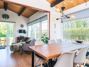 A modern dining area with a wooden table and chairs, large windows, and a ceiling with exposed beams.