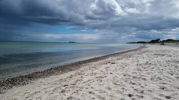 A beach with a pebbly shoreline, calm waters, and a cloudy sky.