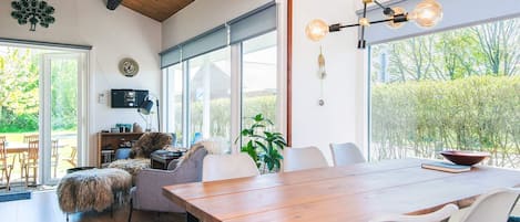 A modern dining area with a wooden table and chairs, large windows, and a ceiling with exposed beams.