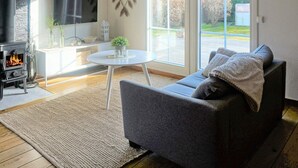 A modern living room with a fireplace, a sofa, a TV, and a large window offering a view of the outdoors. - 7 Person Holiday Home in Solvesborg-by Traum (Sölvesborg)