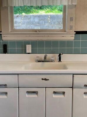 A kitchen with a white countertop, a window with a view of greenery, and a tiled backsplash.