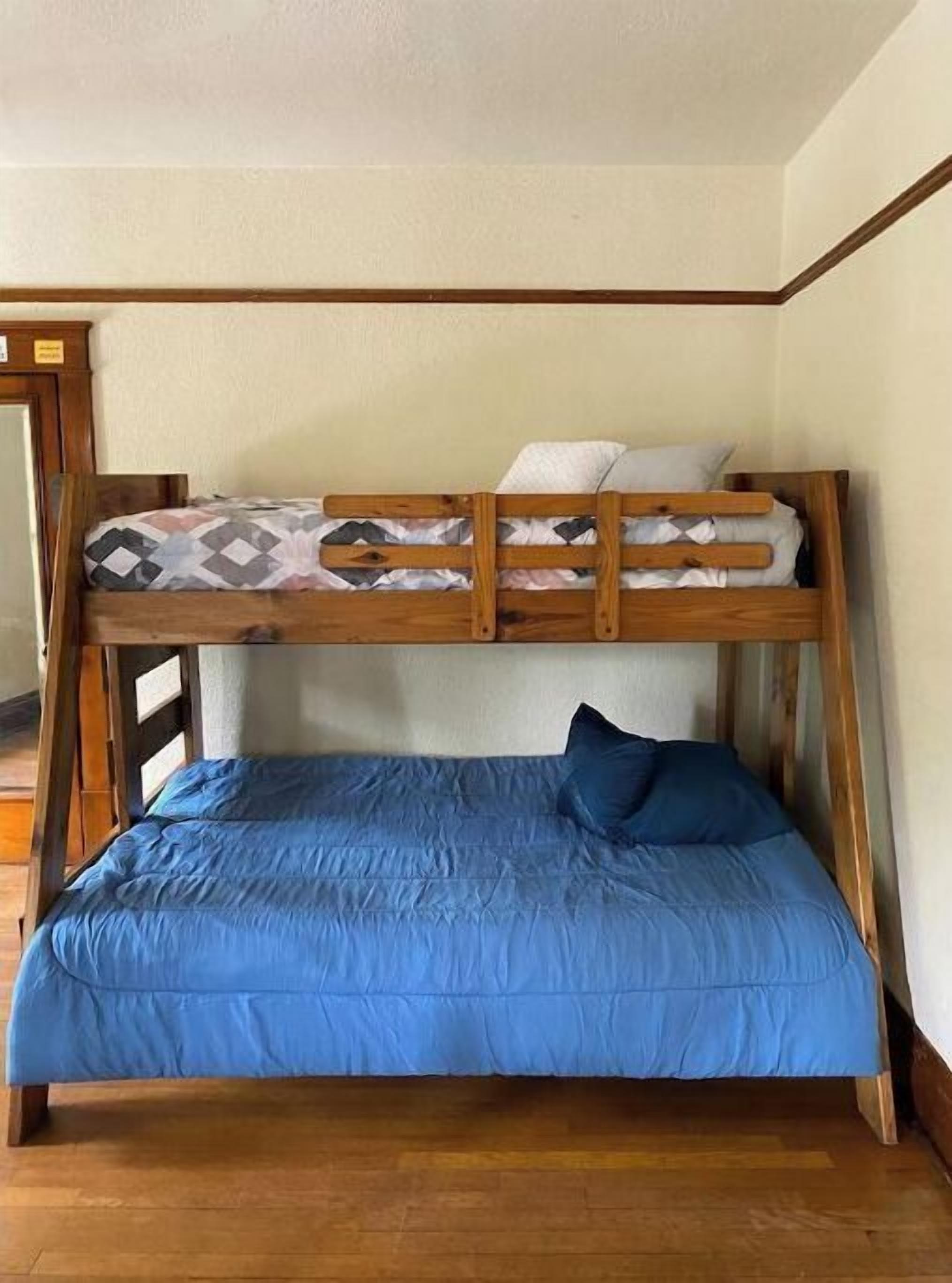 A bunk bed with a lower blue mattress and a top mattress with a patterned blanket.