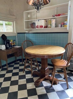 A kitchen with a round wooden table, two chairs, a coffee maker, and a window.