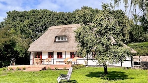 Una casa con techo de paja, un porche y zona de estar al aire libre.