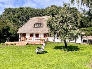 Une maison à toit de chaume, dotée d’un porche et d’un espace extérieur aménagé pour s’asseoir.