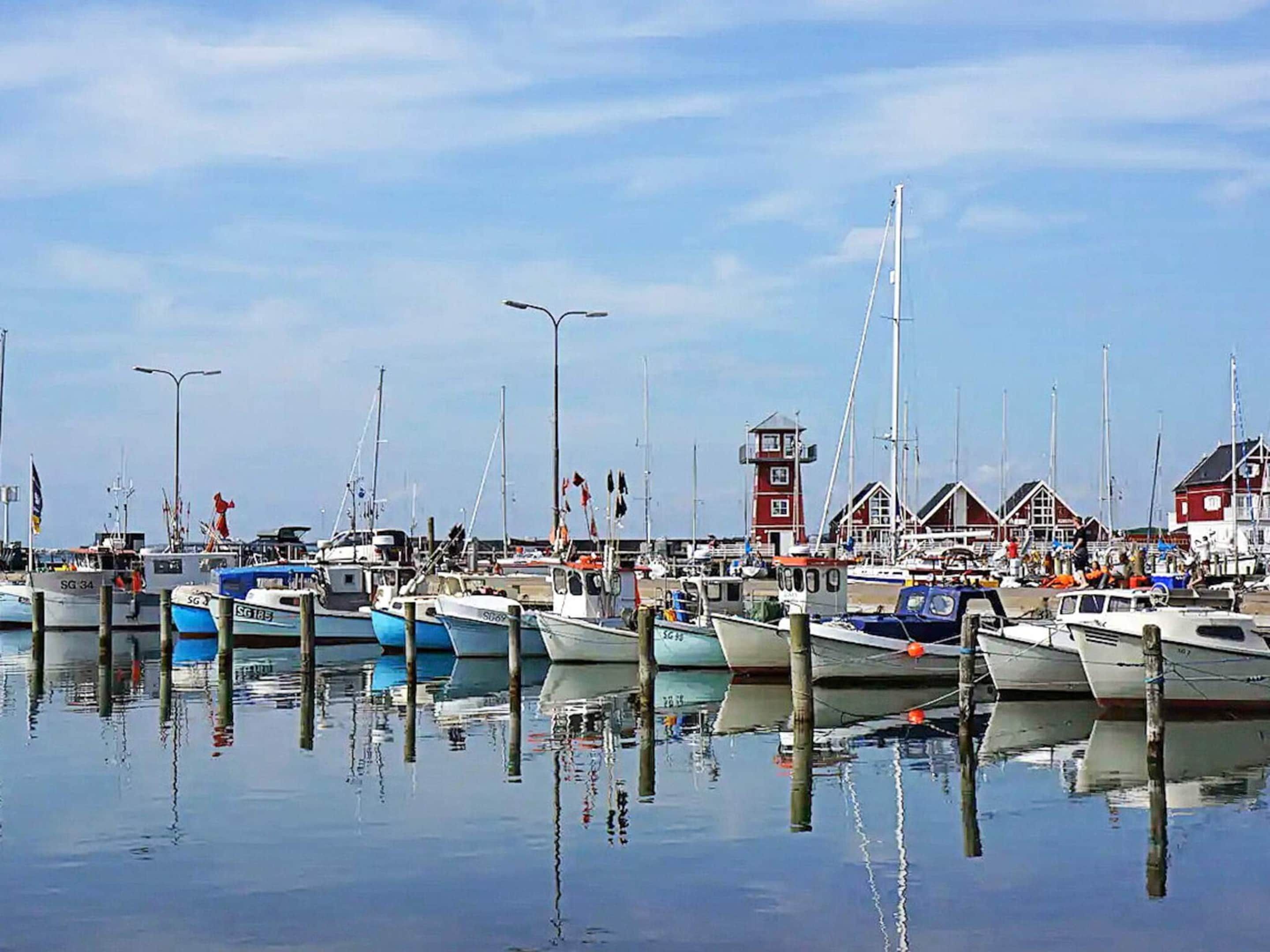 Un port de plaisance avec des bateaux amarrés, un phare et des bâtiments rouges.