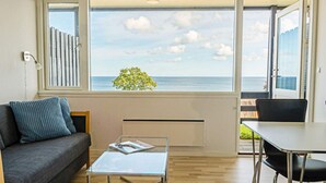 A modern living room with a sofa, a glass coffee table, and a view of the sea through large windows. - 4 Person Holiday Home in Allinge (Allinge)