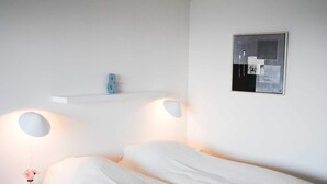 A minimalist bedroom with a bed, bedside lamps, a small shelf, and a framed picture on the wall. - 4 Person Holiday Home in Allinge (Allinge)
