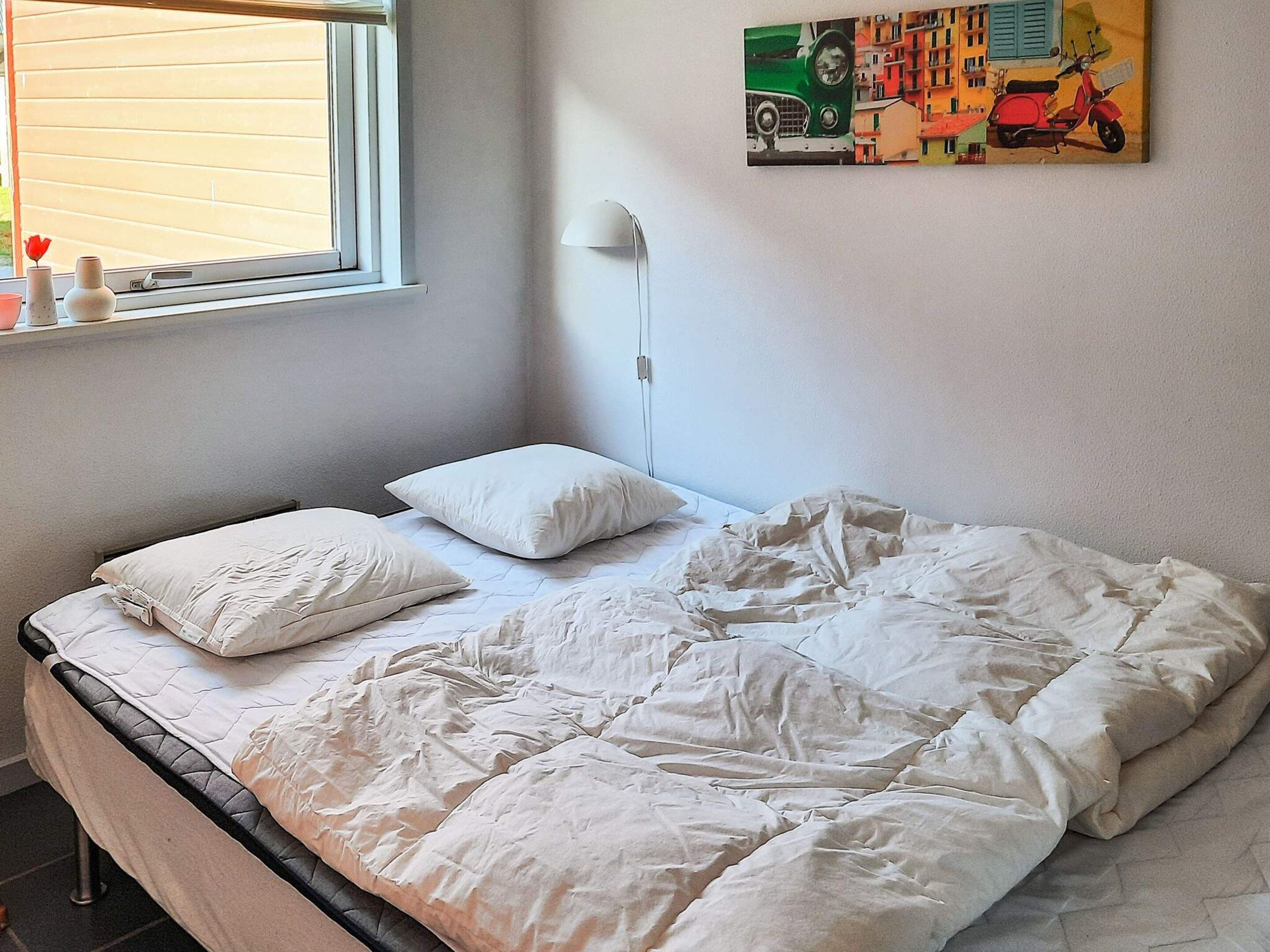 A bed with white bedding, a bedside lamp, and a window with blinds.