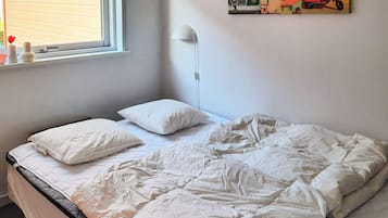 A bed with white bedding, a bedside lamp, and a window with blinds.