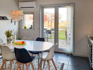 A dining area with a white table, four chairs, and a large window with a view of houses. - 6 Person Holiday Home in Hadsund (Hadsund)