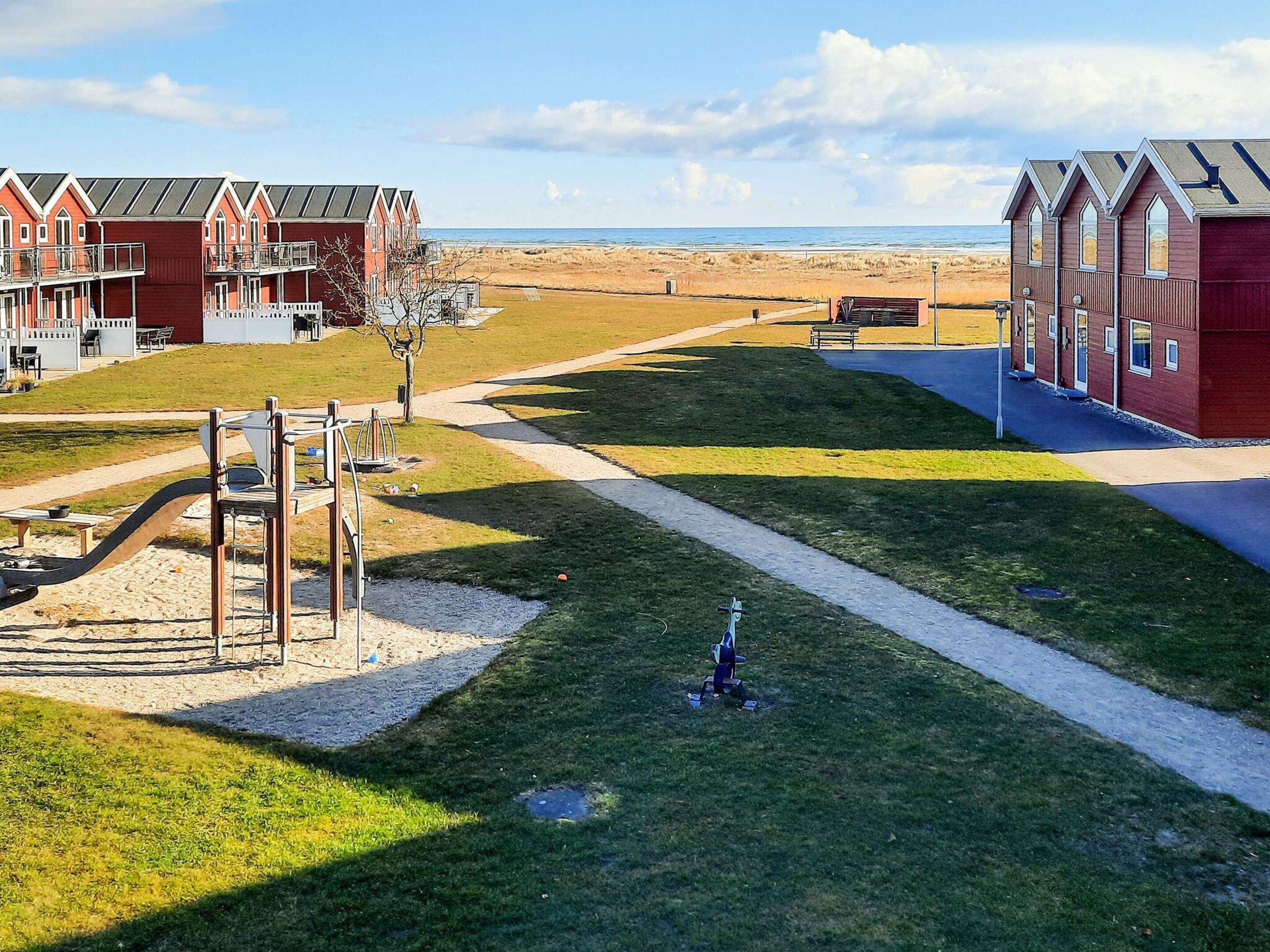 Un hotel frente a la playa con edificios rojos, un parque infantil y una playa de arena al fondo.