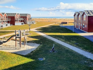A beachfront hotel with red buildings, a playground, and a sandy beach in the background. - 6 Person Holiday Home in Hadsund (Hadsund)