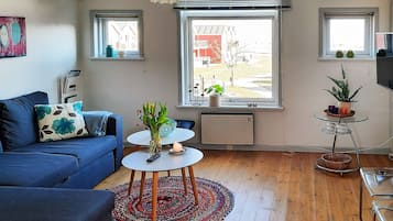 A modern living room with a blue sofa, a round coffee table, and a large window with a view of a building.