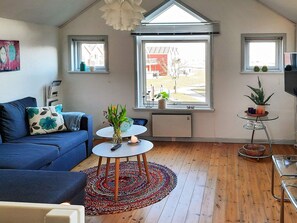 A modern living room with a blue sofa, a round coffee table, and a large window with a view of a building. - 6 Person Holiday Home in Hadsund (Hadsund)