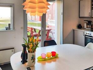 A modern kitchen with a dining table, a vase with flowers, and a view of an outdoor patio. - 6 Person Holiday Home in Hadsund (Hadsund)