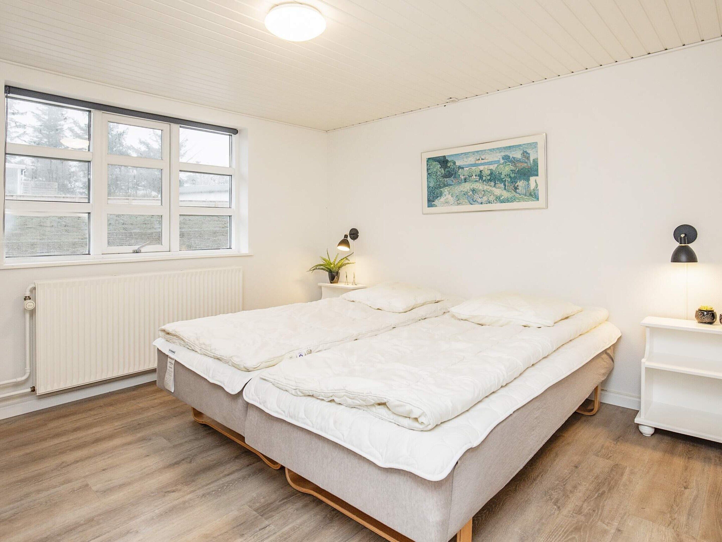 Ein Schlafzimmer mit Bett, Nachttisch, Heizkörper, Fenster und einem Wandbild.