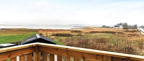 Terraza de madera con vista a un paisaje costero, con el mar y edificios a la distancia.