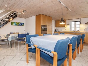A dining area with a long table and blue chairs, a kitchen with wooden cabinets, and a staircase. - 10 Person Holiday Home in Roslev (Roslev)