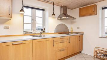 Cocina con armarios de madera, pileta de acero inoxidable, lámparas colgantes y ventana con vista.