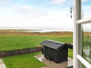 A view from a window overlooking a grassy field with a small black shed and a metal fence. - 10 Person Holiday Home in Roslev (Roslev)