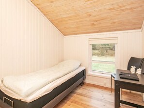 Une petite chambre avec un lit simple, un plafond en bois, une fenêtre donnant sur l’extérieur et un bureau avec une chaise.