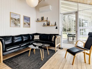 Un salon moderne avec un canapé en cuir noir, une table basse ronde et une chaise en bois. Deux étagères murales sont décorées d'objets d'art.