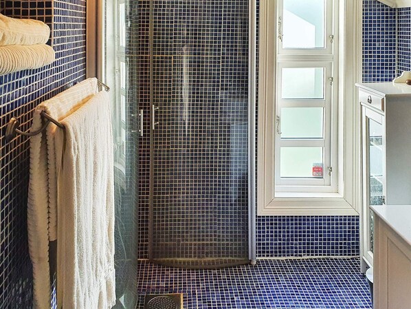 A bathroom with a tiled floor, a shower area, and a window with a view.