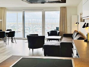 Uma sala de estar moderna com uma grande porta de vidro deslizante que dá para uma vista da cidade, um sofá, uma mesa de centro e uma área de jantar com cadeiras.