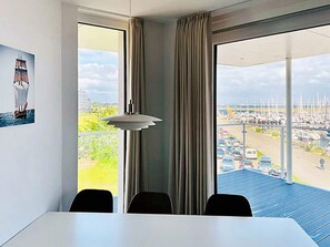 A room with a balcony overlooking a marina, a dining table, and a pendant light.