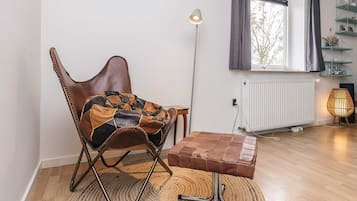 A modern living room with a leather rocking chair, a small wooden table, a floor lamp, and a view of the outdoors through a window.