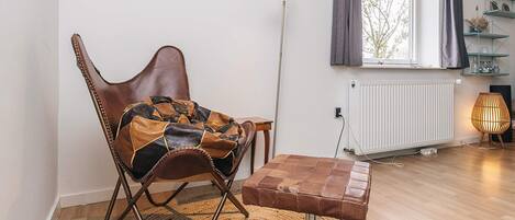 A modern living room with a leather rocking chair, a small wooden table, a floor lamp, and a view of the outdoors through a window.