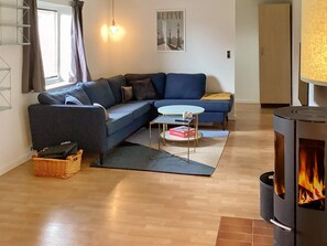 A living room with a sofa, a small round table, a fireplace, and a window with curtains. - 8 Person Holiday Home in Sakskobing (Sakskobing)