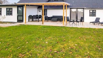 Una casa moderna con un porche cubierto, césped y una terraza.