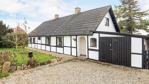 A traditional half-timbered house with a steeply pitched roof, a black door, and a gravel driveway leading to a white entrance. - 8 Person Holiday Home in Sakskobing (Sakskobing)