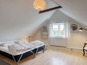 A bedroom with a sloped ceiling, a bed with a patterned duvet, a radiator, a window with curtains, a bedside lamp, and a mirror on the wall. - 8 Person Holiday Home in Sakskobing (Sakskobing)