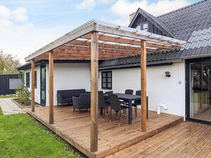 A covered outdoor patio with a wooden pergola, a dining table with chairs, and a white exterior wall. - 8 Person Holiday Home in Sakskobing (Sakskobing)