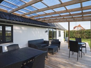 A covered outdoor patio with a table and chairs, a sofa, and a glass enclosure. - 8 Person Holiday Home in Sakskobing (Sakskobing)