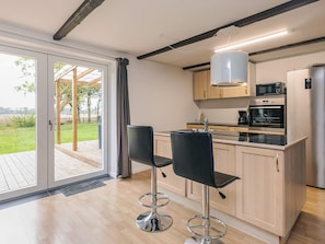 A modern kitchen with a built-in oven, microwave, and coffee maker. There are two black bar stools and a sliding glass door leading to a patio. - 8 Person Holiday Home in Sakskobing (Sakskobing)