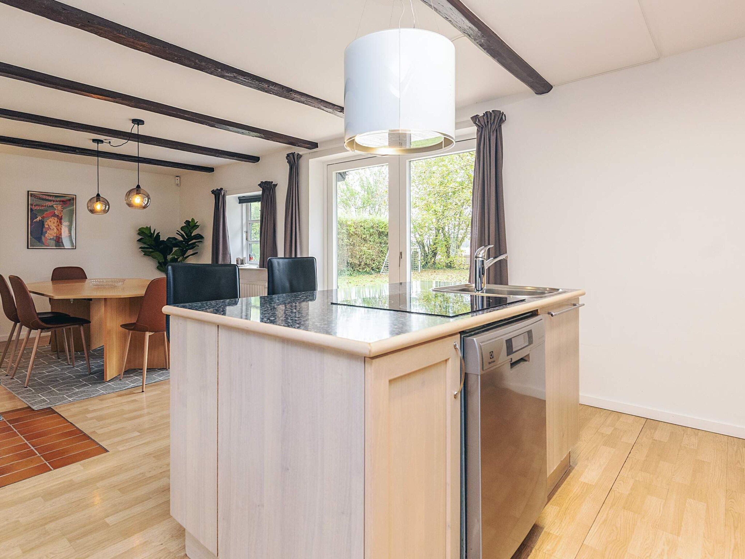 A modern kitchen with a central island, built-in dishwasher, and a window with curtains.