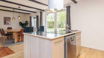 A modern kitchen with a central island, built-in dishwasher, and a window with curtains.