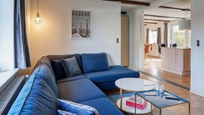 A modern living room with a sectional sofa, a round coffee table, and a dining area in the background. - 8 Person Holiday Home in Sakskobing (Sakskobing)
