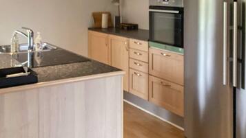 A modern kitchen with wooden cabinets, a stainless steel refrigerator, and a built-in oven.