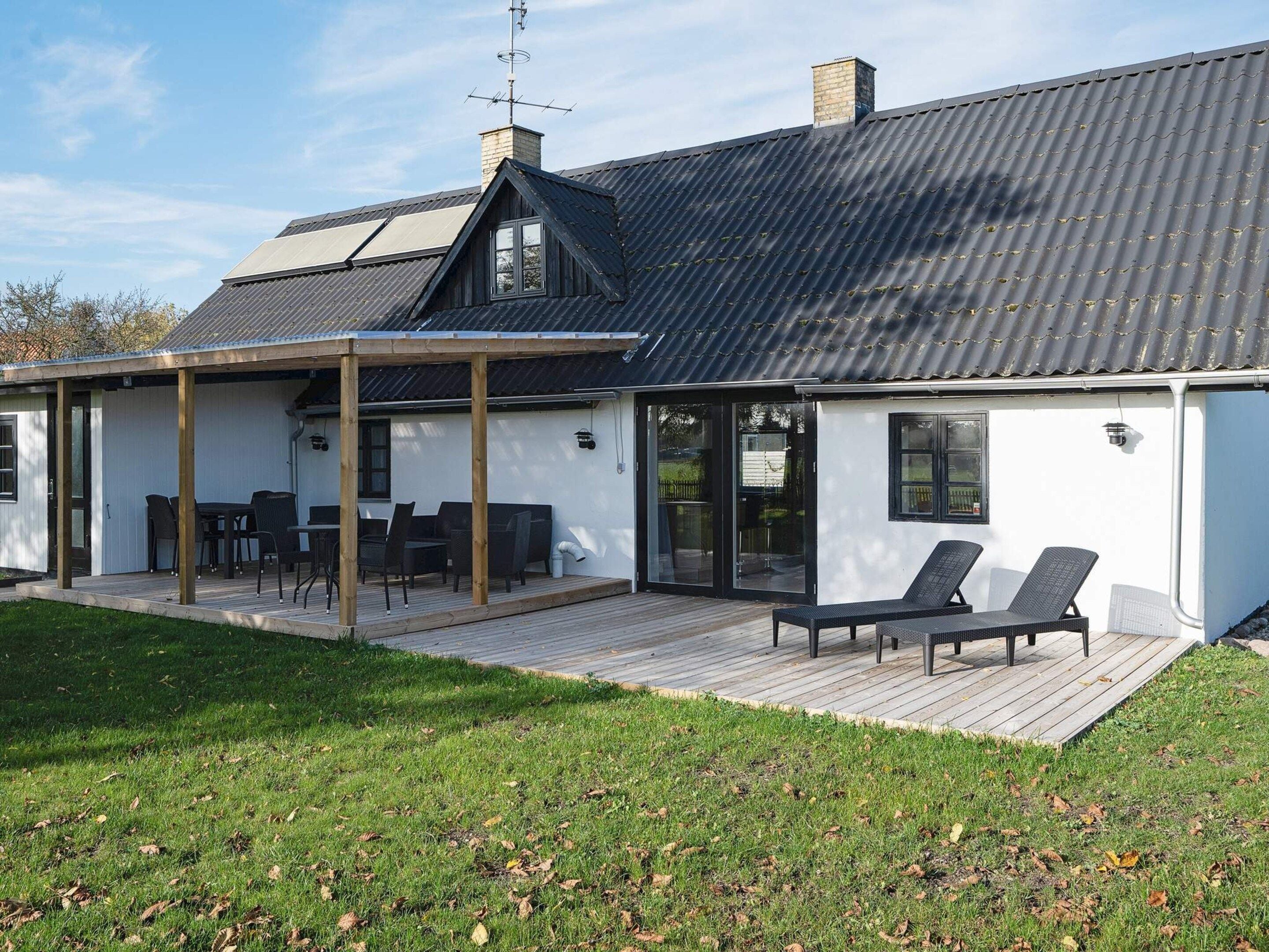 A modern house with a covered patio, a chimney, and a deck with outdoor furniture.